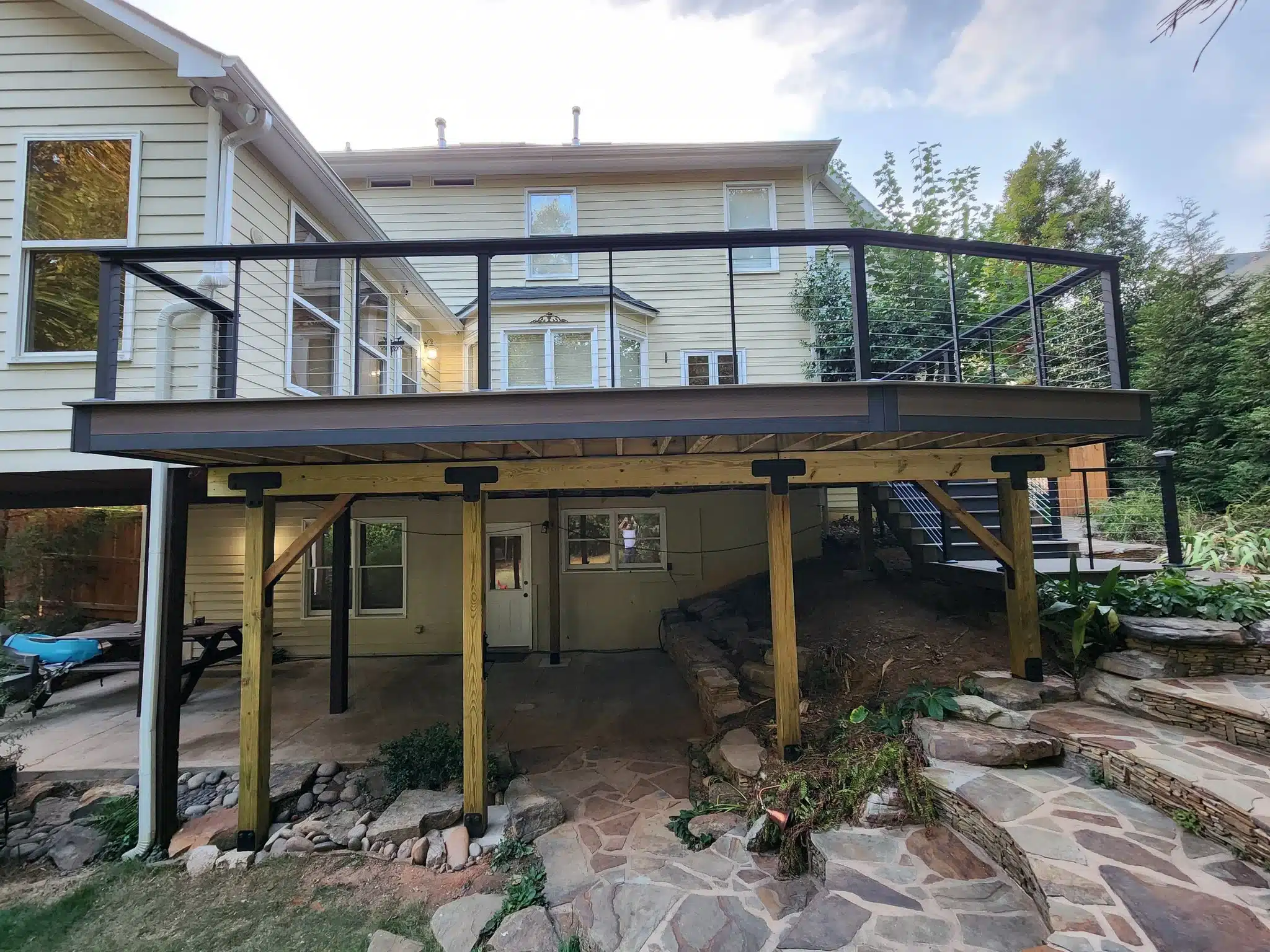 Uplift composite deck with modern cable railing and natural stone patio below.