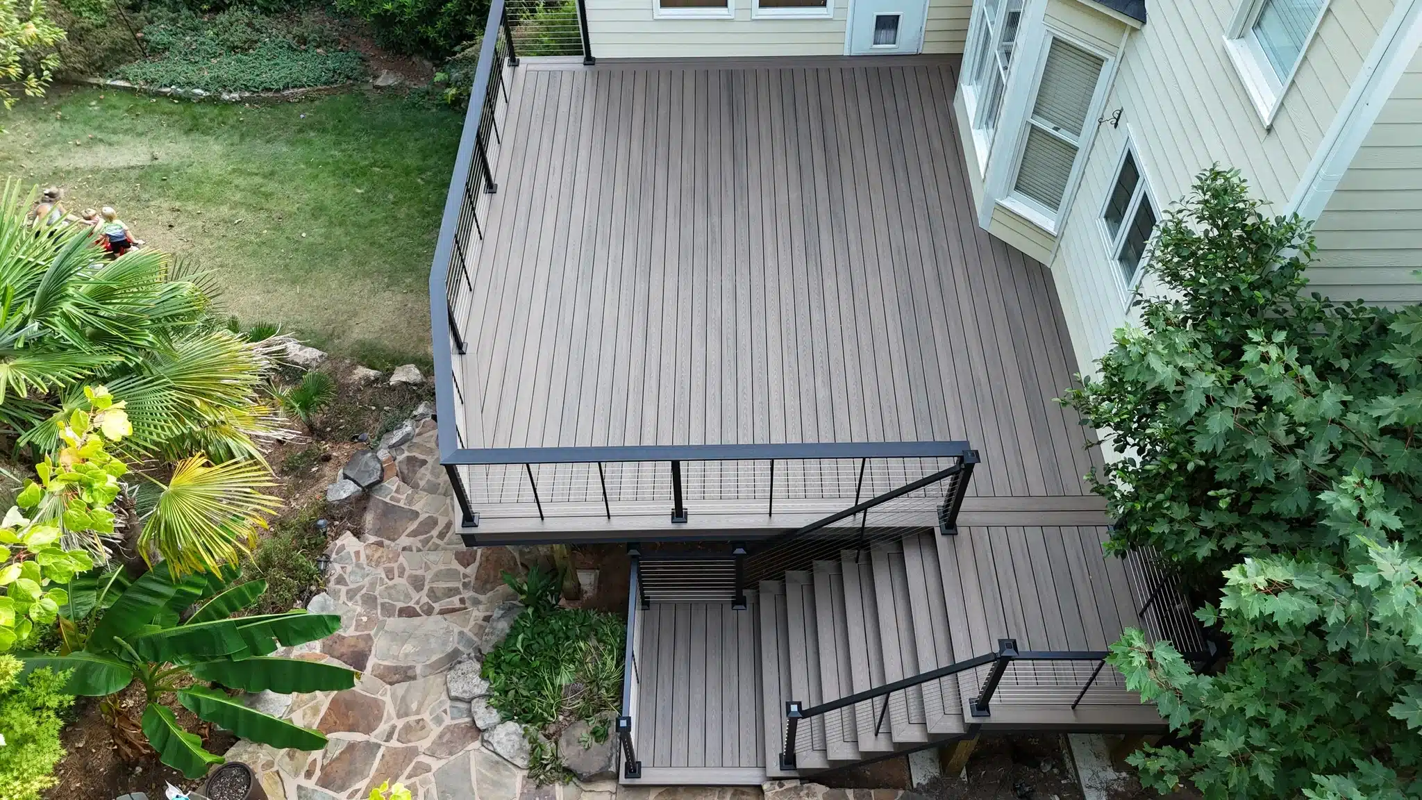 Composite deck with sleek cable railing and stairway leading to natural stone path.