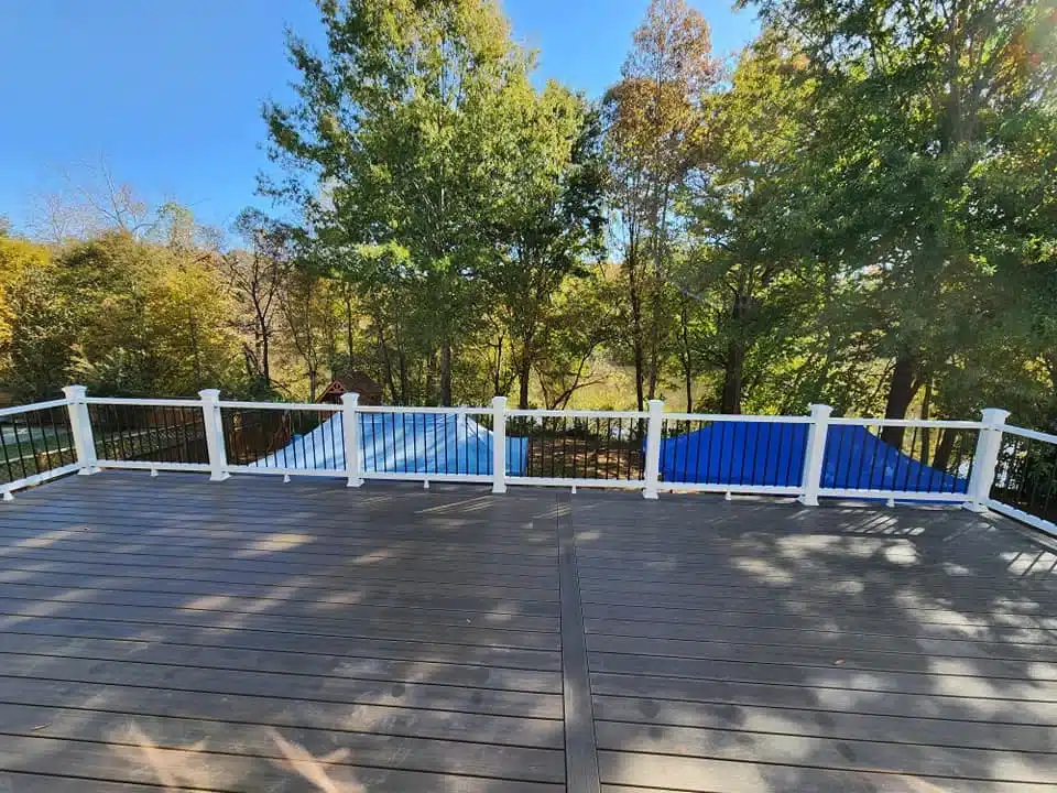 Composite deck with white and black railing overlooking wooded backyard.