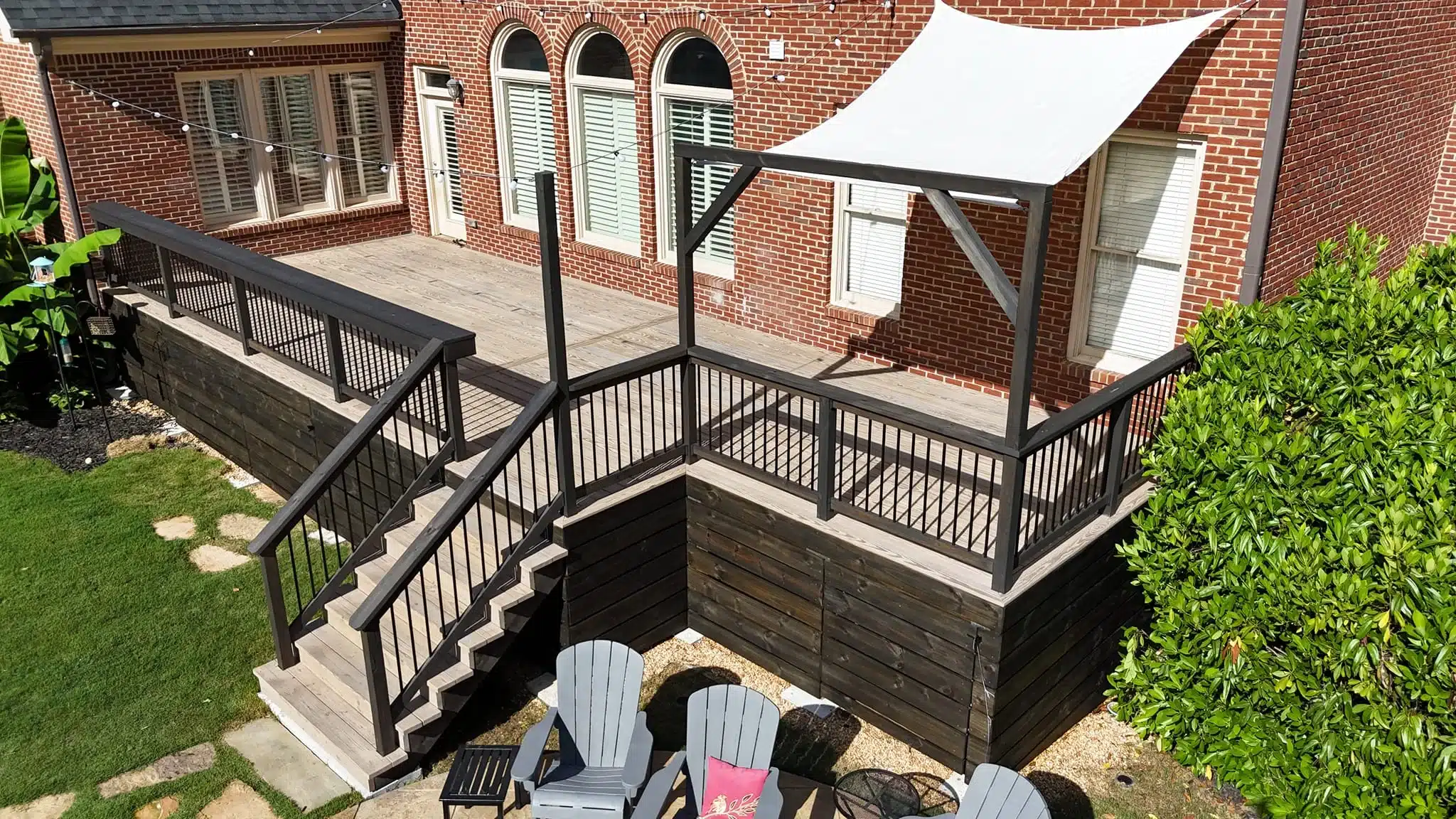 Elevated wood deck with dark railing, stair access, sail shade, and built-in string lighting.